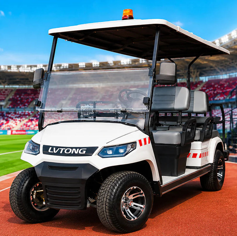 A white and black LV TONG electric golf cart with an orange beacon light is parked on a red track next to a stadium building with a medical room sign. In the background, a soccer stadium with red seats and a stretcher with medical supplies is visible under a blue sky.